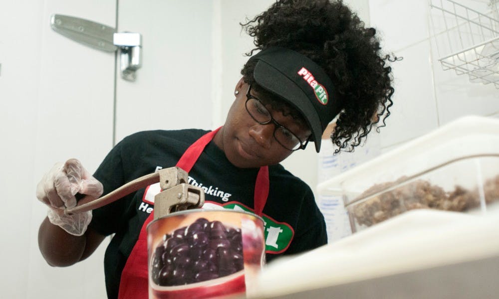 <p>Elementary education junior Kayla Jackson opens a can of olives on Sept. 23, 2015, at Pita Pit, 219 E. Grand River Ave., in East Lansing. Kayla stocked the back room and provided replacements when certain ingredients ran out during her shift. Kennedy Thatch/The State News</p>