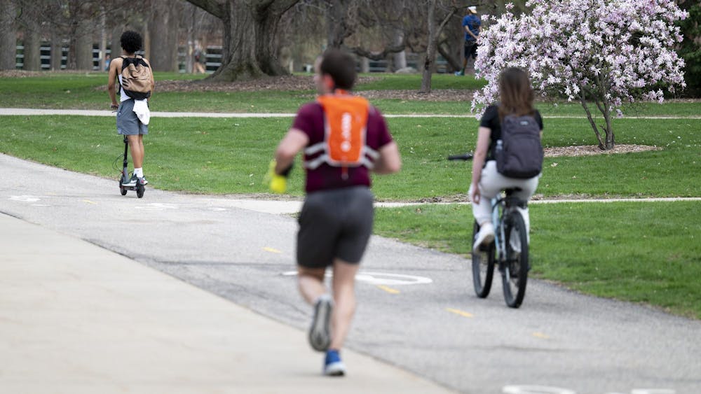 Person riding a scooter along the river trail while Spartans bike and run at Michigan State University campus on April 14, 2025