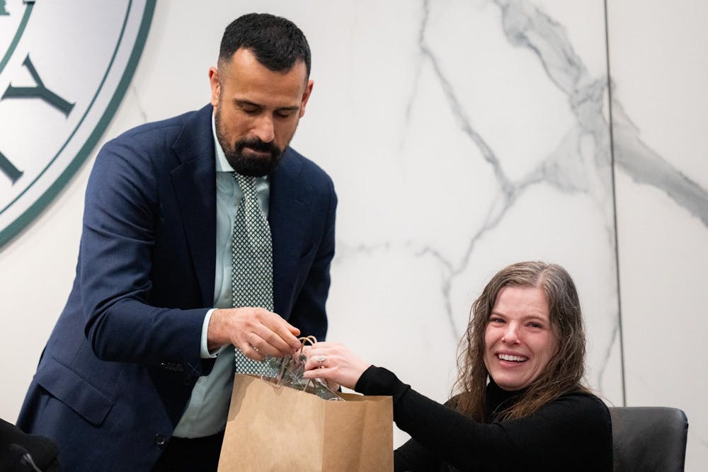 <p>MSU Board of Trustees secretary Stefan Fletcher hands a bag to Vice Chair Kelly Tebay to celebrate Tebay's time on the board at Hannah Administration Building in East Lansing, Michigan on Friday, Dec. 12, 2025. </p>