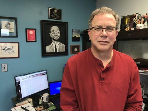 A person smiles and poses for a picture while standing in an office.