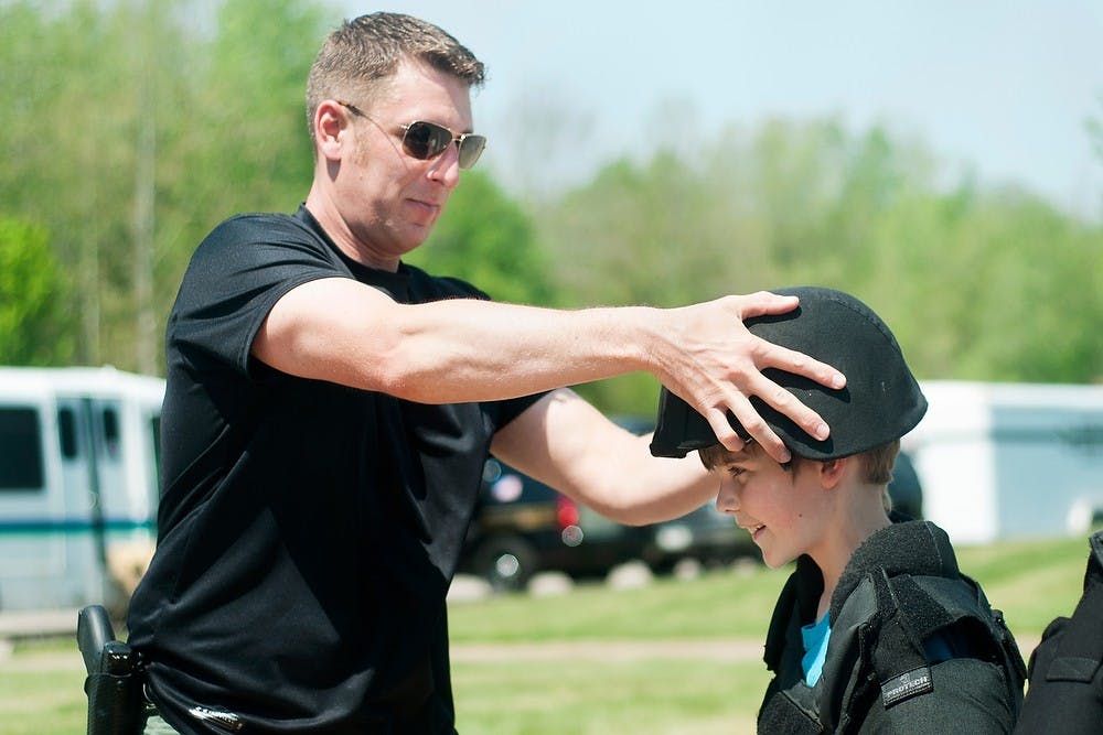 	<p>Lansing Police Sgt. Ryan Wilcox of the Special Tactics and Rescue Team, places a kevlar helmet on Webberville, Mich., resident Christopher Kemler, 10, at the annual Police and Fire Field Day and Safety Patrol Picnic, on May 15, 2013, at Hawk Island Park, 1601 E. Cavanaugh Road, in Lansing. The event was hosted by the Lansing Area Safety Council to teach kids about public safety. Danyelle Morrow/The State News</p>