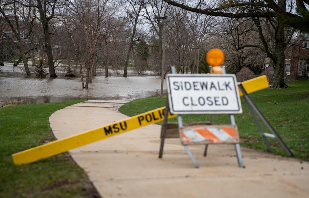The sidewalk is closed as the Red Cedar River floods it after heavy rainfall on campus on April 5, 2023. 