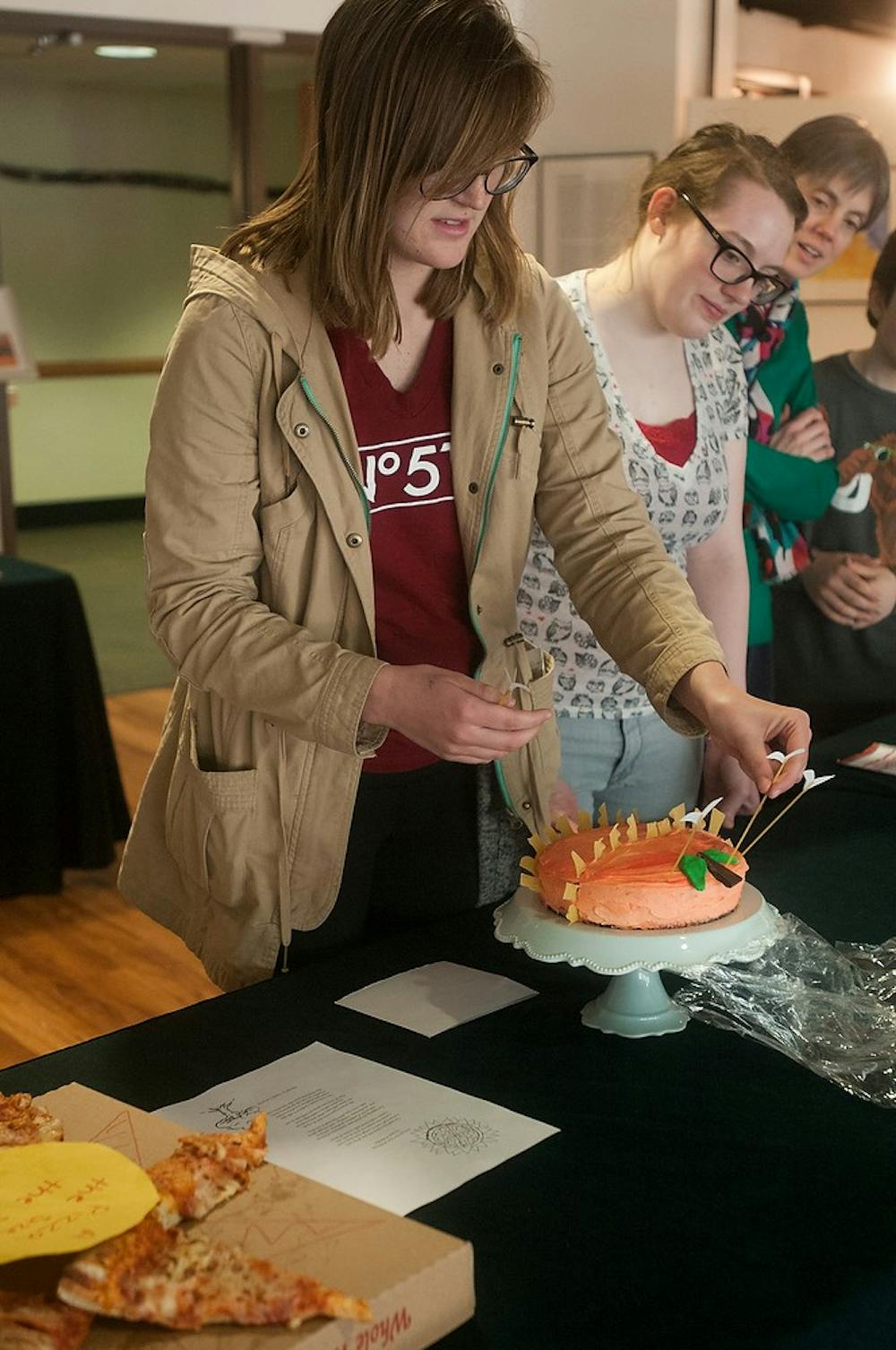 <p>Arts and humanities senior Darby McGaw puts the finishing touches on her James and the Giant Peach inspired cake April 1, 2015, at the Center for Poetry's Edible Book Contest hosted by the Residential College in the Arts and Humanities. McGaw's cake won best in Children's Literature. Kennedy Thatch/The State News  </p>