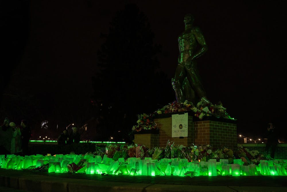 <p>Green-lit luminaries, flowers, and supportive messages surround the Spartan Statue on Feb. 13, 2024. One year after the Michigan State University campus shooting, a remembrance ceremony was held to remember and reflect on the tragedy.</p>