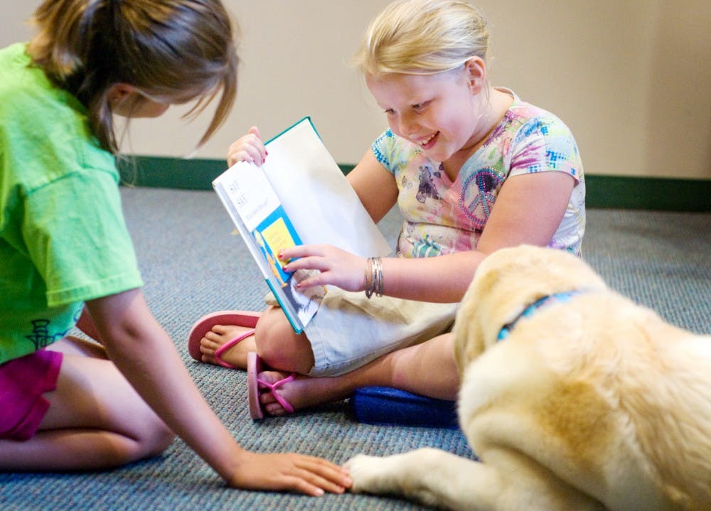 	<p>Lansing resident Gloria Zink, 7, center, reads to her sister Lilly, 10, and Mason resident Mary Mulder&#8217;s dog Lilly Monday at East Lansing Public Library, 950 Abbot Road. Mulder and her dog participate in Therapy Dogs International which brought in two other dogs for children to read to Monday afternoon.</p>