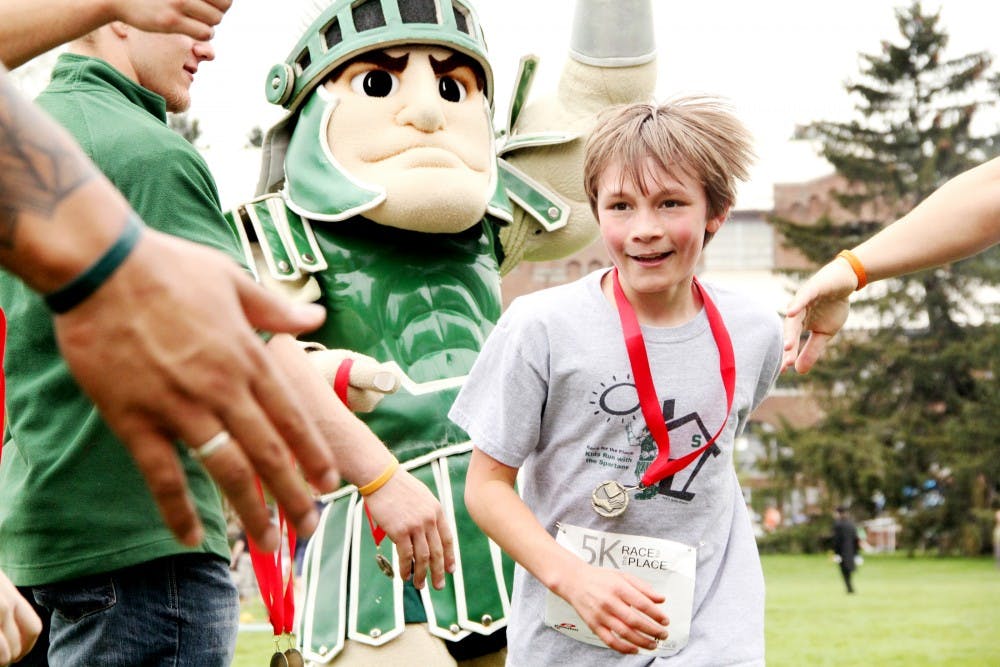 Dax Summers, 10, runs through the finishline to be greeted and congratulated by MSU athletes and Sparty after running in the 1 mile kids race which is part of the Race for the Place 5K fundraiser Sunday afternoon at Demonstration Field. MSUFCU sponsored the annual Race for the Place 5K and all proceeds benefit MSU Safe Place. Aaron Snyder/The State News. 