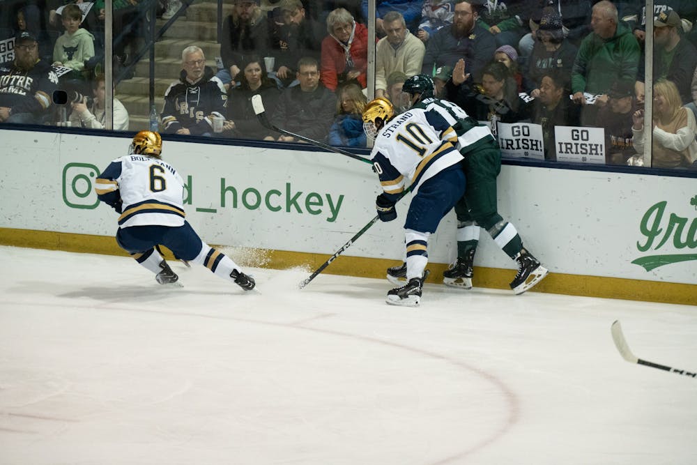 <p>Notre Dame defenseman Jake Boltmann (left) kicks up snow as he turns near the boards while center Hunter Strand finishes a hit on MSU winger Miroslav Mucha at Compton Family Ice Arena in Notre Dame, IN on Friday, March 4, 2023. Boltmann recorded 4 blocked shots in the 4-2 loss to MSU.</p>