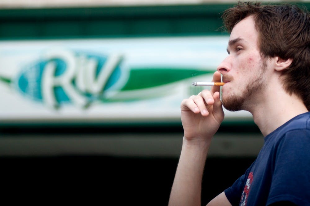 Anthony Corbin, Holt resident, smokes a cigarette on Tuesday outside of The Riv, 231 M.A.C. Ave. As a smoker, Corbin does not support the Michigan Smoke-Free Air Law that was passed in May of 2010, which prohibits smoking in most public places in Michigan. "You don't go to the bar for a healthy experience. You go there to smoke and drink, and I dig the smoky atmosphere," Corbin said. Mo Hnatiuk/The State News