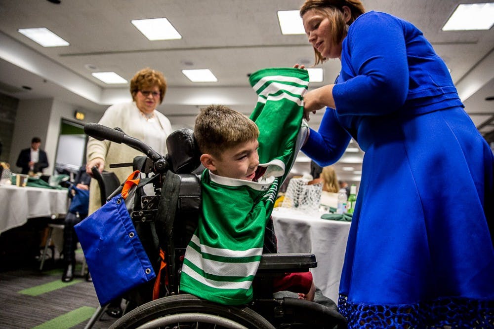 <p>Jill Willimeth helps her son Connor, 7, put a signed jersey on during the MSU Men's Lacrosse Ring Ceremony on Dec. 1, 2018 at the Breslin Center.</p>
