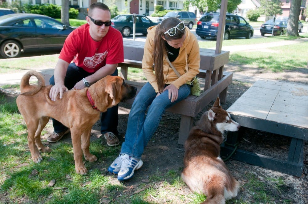 MSU alum Taylor Bond, left, and biomedical laboratory sciences junior Melissa Rust play with dogs Otis and Remmington Sunday afternoon outside a home on M.A.C. avenue. The pair were waiting while their friends were grilling hotdogs. Julia Nagy/The State News