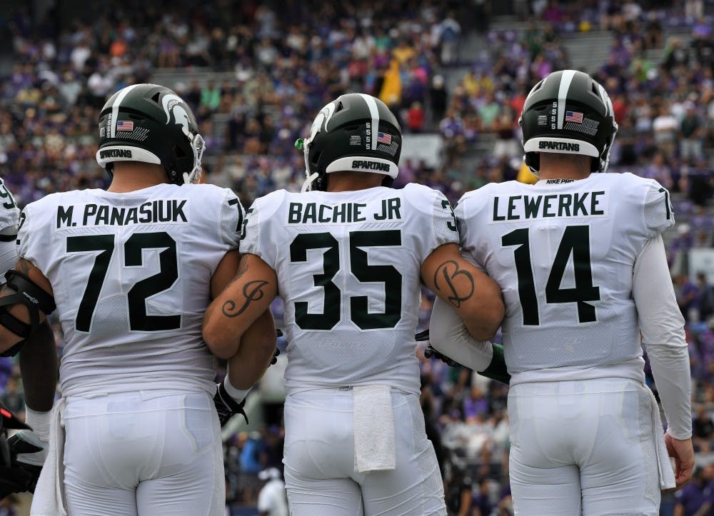 <p>Seniors Mike Panasiuk (72) (left), Joe Bachie Jr. (35) (middle) and Brian Lewerke (14) (right) lock arms before the game against Northwestern on Sept. 21, 2019 at Ryan Field. MSU defeated Northwestern, 31-10.</p>