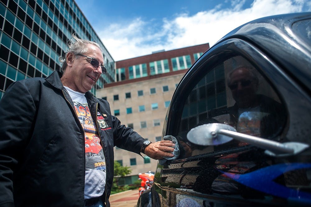 	<p>Denny Lawrason, of Flushing, Mich., wipes his car dry after a rain shower, July 27, 2013, in downtown Lansing during the Car Capital Auto Show 2013. The 21st annual event was organized by the R.E. Olds Transportation Museum. Justin Wan/The State News</p>