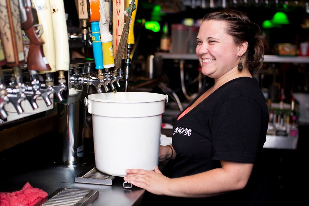 East Lansing resident and Crunchy's bartender Alicia Garnero prepares a bucket of The Locals Light Beer crafted by Short's Brew located in Bellaire, Mich., on Sunday night. Garnero said the bucket sells for around $29 and is about the same as drinking a 24-pack of beer. Natalie Kolb/The State News