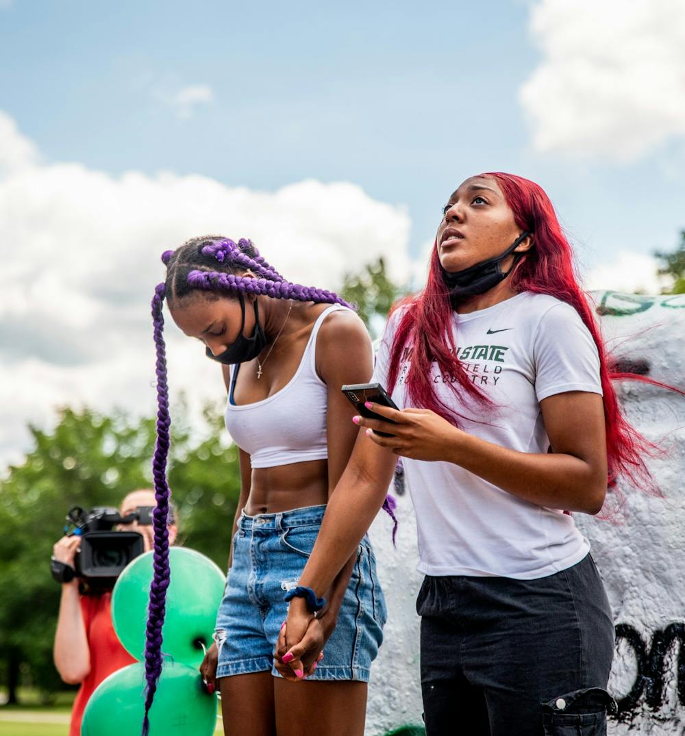 Jaiden Paris (right) looks up as she reads a prayer at the memorial for long jumper Tony Martin while Asya Reynolds (left) holds her hand at the Rock on Farm Lane July 20, 2020. Martin died in a shooting in his hometown of Saginaw the morning of July 19. Martin held the high school state record for the long jump, with a jump of 26 feet and six inches.