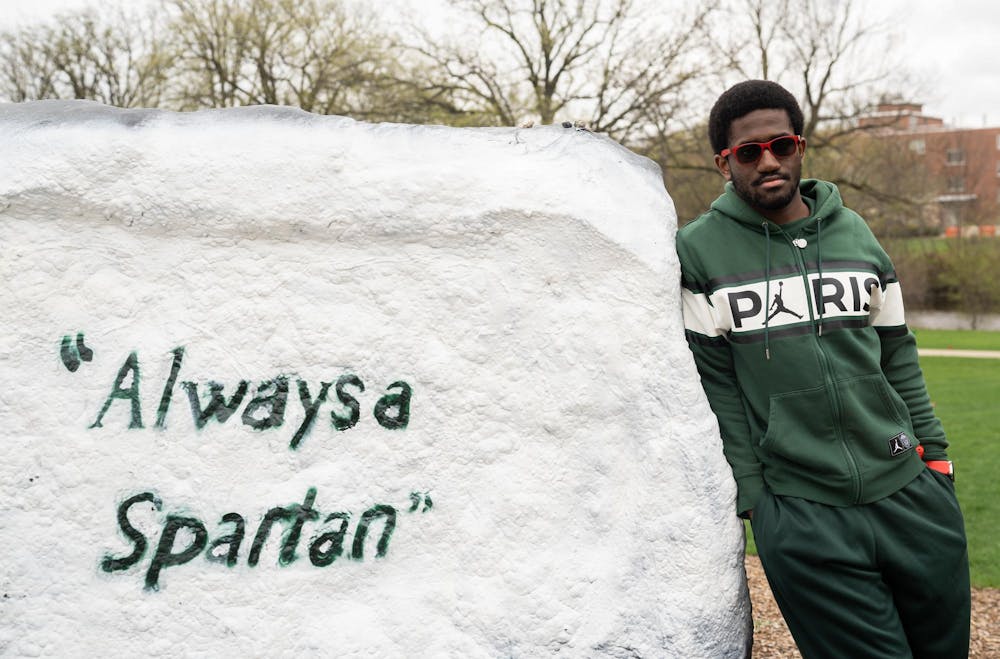 Computer science senior Dorian Smalley poses for a photo next to the Rock on Farm Lane on Friday, April 21, 2023. The Rock has become a symbol of unity to Smalley in the aftermath of the Feb. 13 shooting on MSU’s campus, and it reminds him not to take family and friends for granted.