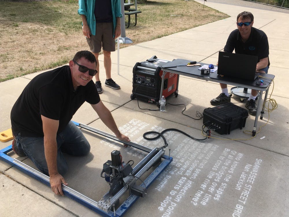 <p>Don Easlick and Ralph Hansel of Endless Engravings in Charlotte, Michigan, etch a contest-winning poem into a Lansing sidewalk. <strong>Photo courtesy of Ruelaine Stokes.</strong></p>