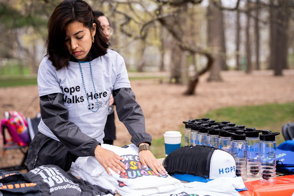 CAPS staff member Jessica Oyoque-Barron organizes a stack of t-shirts that read "WE CAN STOP SUICIDE" at the "Out of the Darkness" walk for suicide prevention on Sunday, April 16, 2023. The event, a collaboration between CAPS and the American Foundation for Suicide Prevention culminated in a "walk of hope and healing."