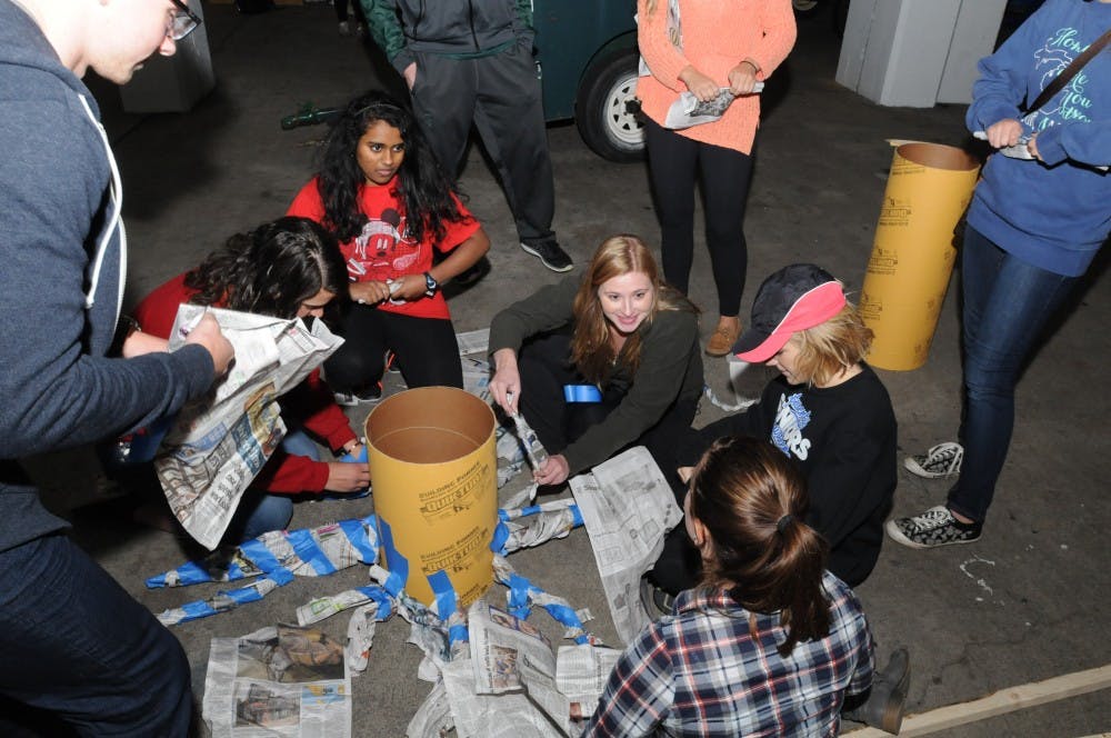 <p>From left to right, kinesiology sophomore Lauren Eilbeck, physiology sophomore Divya Venkatesan, marketing sophomore Kristen Hetzel, social work sophomore Krystle Baecker and psychology sophomore Marissa Jacks sit and fold newspapers for their Tower Guard float on Sept. 30, 2015, at Spartan Stadium. The group was building a float for homecoming. </p>