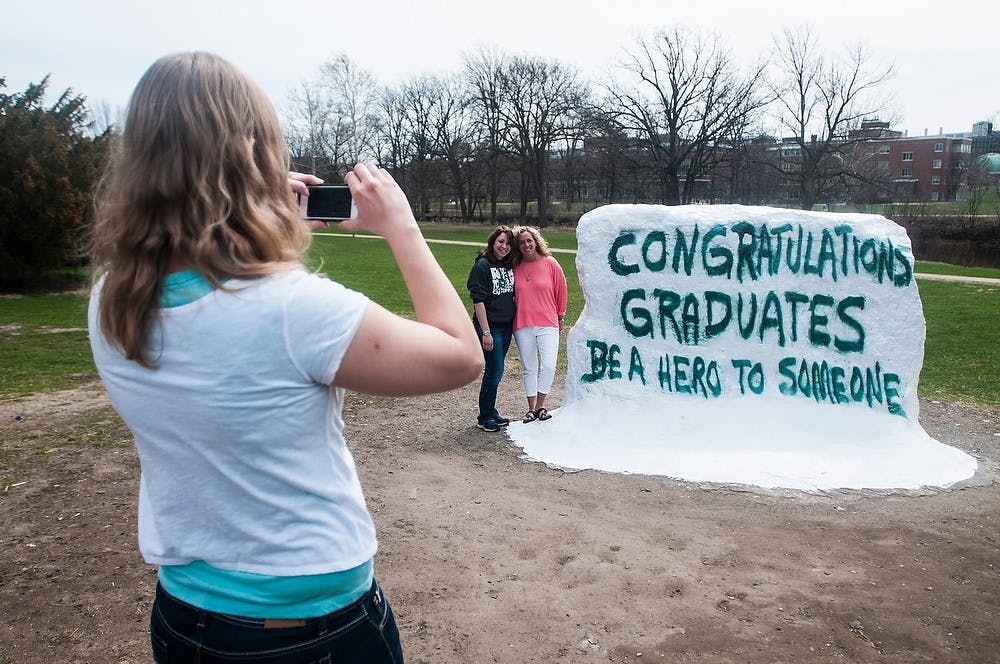 <p>Graduate student Kelsey Lehman takes a photo of graduate students Deanna Burbank, left, and Deanna Swan on April 21, 2014, at the Rock on Farm Lane. The Rock was previously painted in memory of Lacey Holsworth with messages from Spartans on it. Erin Hampton/The State News</p>