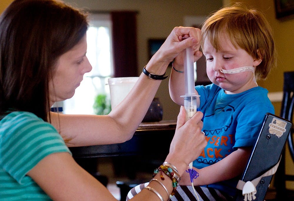 	<p>Charlie Waller, 3, helps his mother, Abigail, push a dietary supplement through a feeding tube that runs across his face and into his stomach Aug. 30, 2011, morning in their East Lansing home. With Charlie&#8217;s high fat, or ketogenic, diet, he must find ways to add more fat aside from the food he eats. The dietary supplement helps to increase the amount of fat he ingests, but tastes terrible, so it is given to Charlie through his feed tube. Matt Radick/The State News</p>