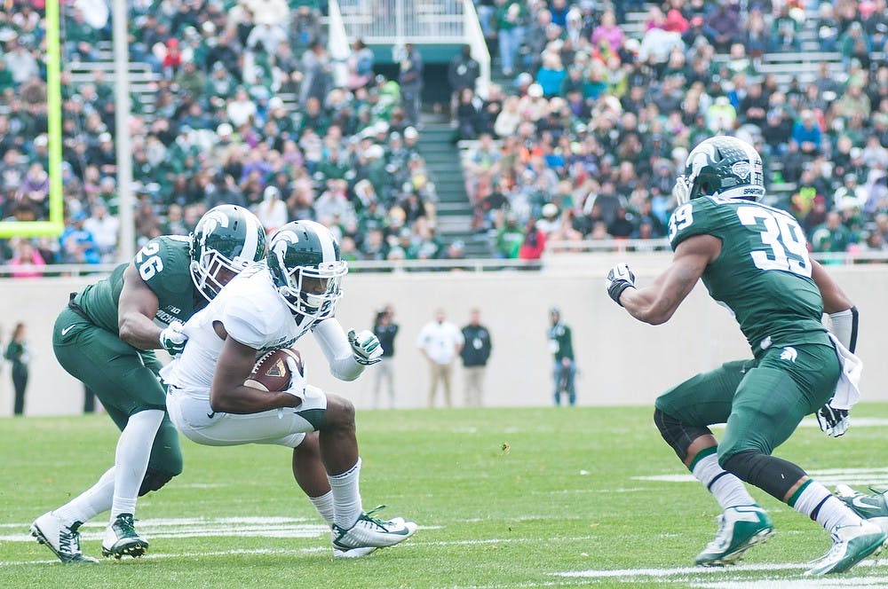 <p>Senior wide receiver DeAnthony Arnett holds onto the ball while senior safety RJ Williamson and junior cornerback Jermaine Edmondson try to tackle him during the Spring Green and White game April 25, 2015, at Spartan Stadium. The white team defeated the green team, 9-3. Hannah Levy/The State News</p>