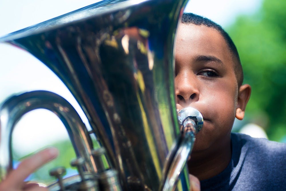 <p>Lansing resident Elijah West, 9, is taught how to play the tuba during the Juneteenth Festival on June 21, 2014, at St. Joseph Park in Lansing. Haslett, Mich., resident Marissa Olin had a table at the festival filled with instruments for people to try. Hayden Fennoy/The State News</p>