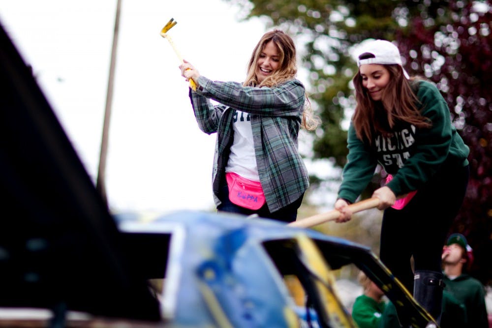 From left, advertising sophomore Ally Fiteny and business sophomore Courtney Zotis smash the roof of a car Saturday morning at the Delta Chi Fraternity house. The brothers at Delta Chi collected a fee to crush the car which was donated to cancer research. Matt Hallowell/The State News