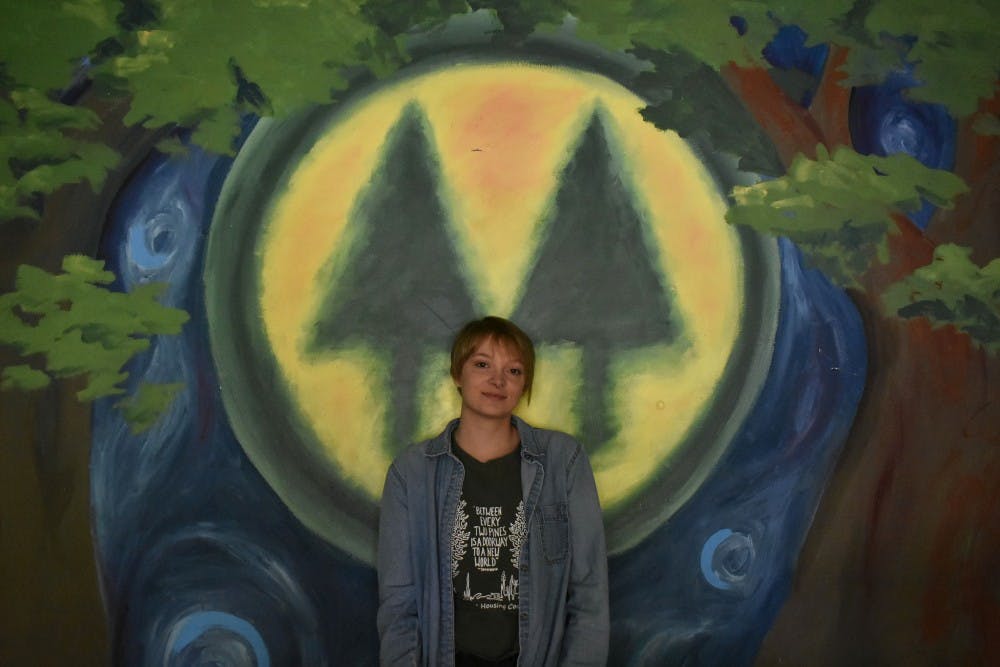 <p>Dix poses in front of SHC&#x27;s logo which is painted in the Tree Room. A drum set and phone booth serve as decorations for the Tree Room.</p>