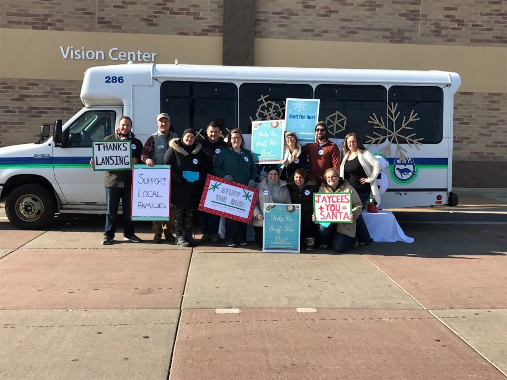 <p>Volunteers hold signs in front of a bus to be filled with gifts at Walmart in the Eastwood Towne Center in Lansing. <strong>Photo courtesy of JCI Lansing</strong></p>