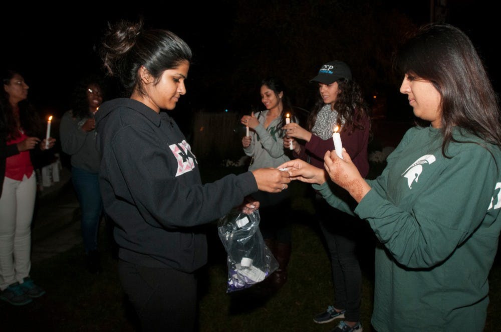 <p>From left, psychology and communication senior Priya Adusumilli, president of Sigma Sigma Rho, gives human resource management junior Sakshi Sethi a paper with a fact about domestic violence to read aloud during a Sigma Sigma Rho Sorority event on Oct. 21, 2015 at the Sparty Statue. The sorority lit luminaries in support of domestic violence victims.</p>