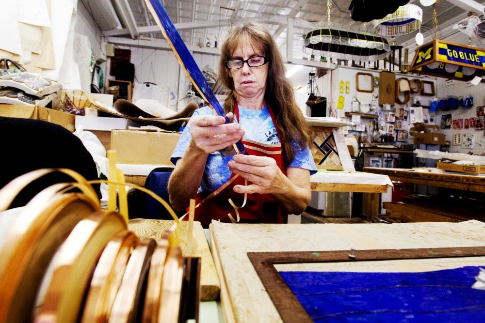 (Above) Owner of Lansing Art Glass Linda Stevens wraps a piece of glass in copper adhesive Monday afternoon at her Lansing storefront. Stevens has been working with glass since she enrolled in a stained glass class at Lansing Community College in 1981. (Below) Lansing Art Glass owner Linda Stevens grinds down a piece of glass so it fits perfectly into a collage Monday afternoon at her shop. Matt Hallowell/The State News. Matt Hallowell/The State News. 