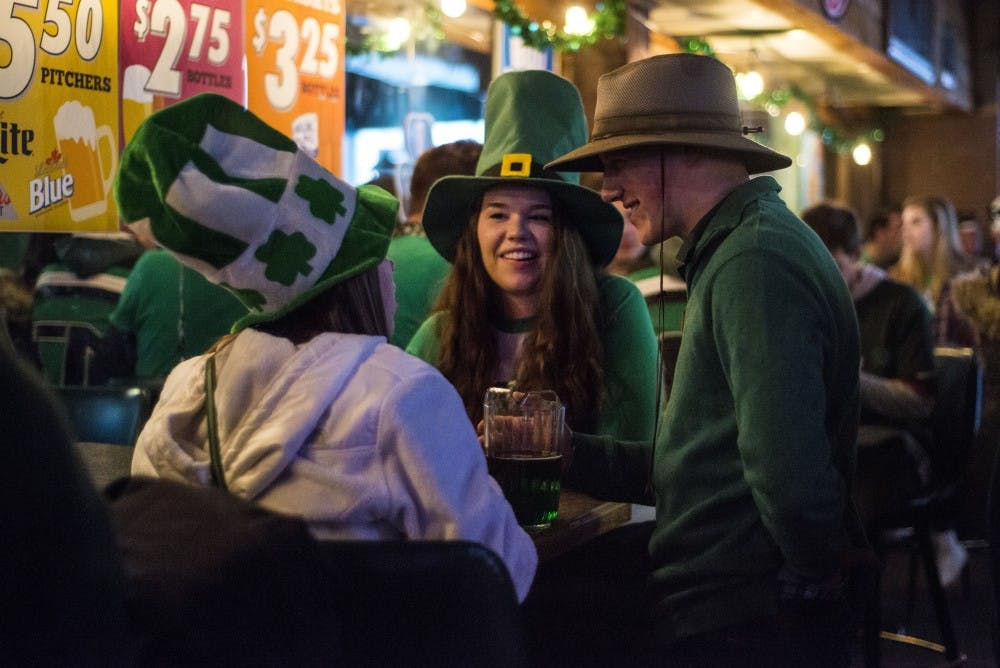 From left to right, environmental biology senior Renee O'Connell, zoology junior Megan White and chemical engineering senior Kevin Klebba converse during St. Patrick's Day on March 17, 2017 at P.T. O'Malley's at 210 Abbot Road in East Lansing.