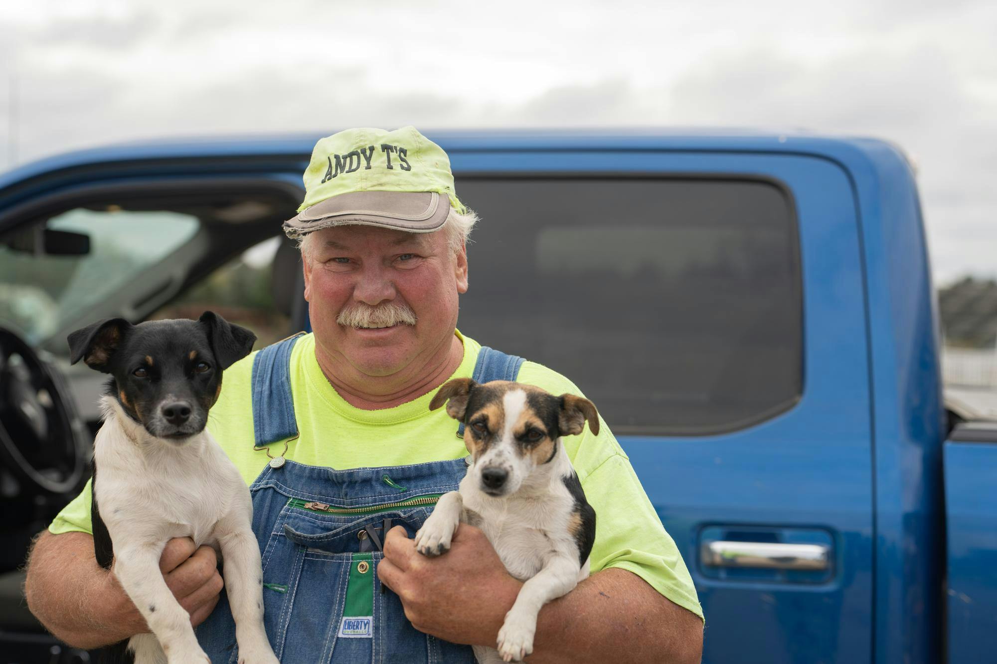 <p>Andy T's Farm Market namesake Andy Todosciuk stands with his dogs Buck (left) and Solo (right) on Sept. 29, 2024. He tries to visit every bonfire his farm hosts, often with a canine in tow.</p>