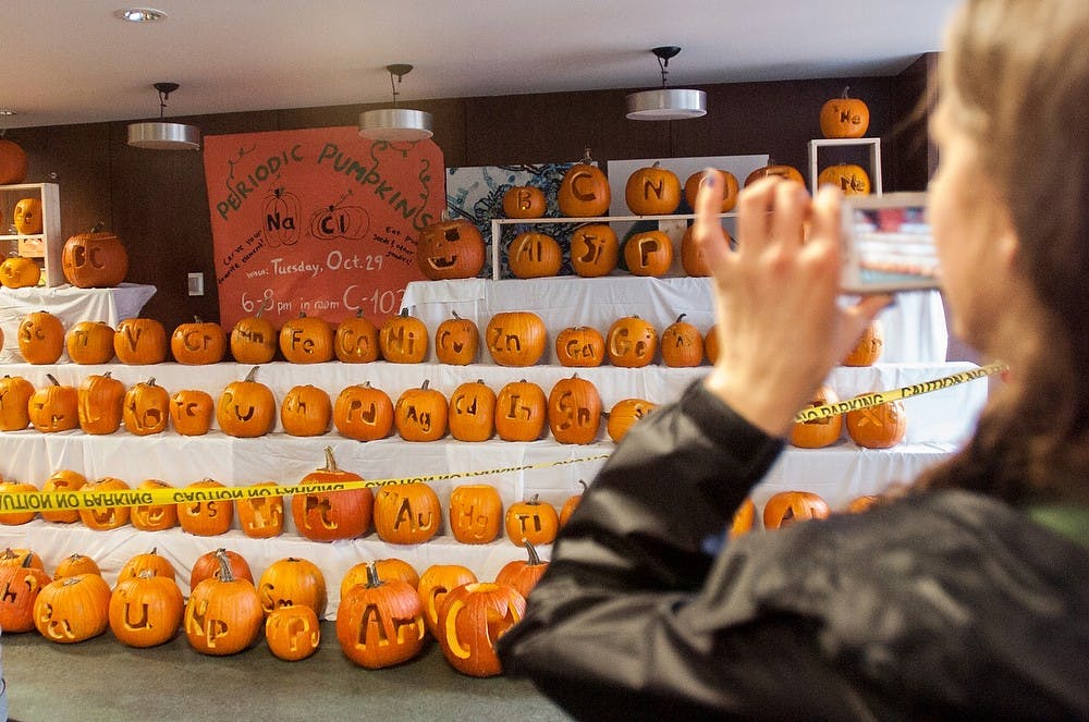 	<p>Human biology sophomore Rachel Rosinski takes a photo of a periodic table made out of pumpkins Oct. 31, 2013, near the entrance of West Holmes Hall. The pumpkins were carved by residents of West Holmes Halls and students of Lyman Briggs College to celebrate Halloween and their love of science. Olivia Dimmer/The State News</p>