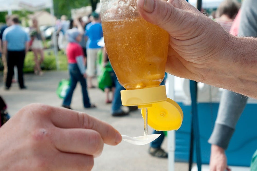 	<p>Fowlerville, Mich., resident Dale Woods, right, pours honey on Lansing resident Gary Newton&#8217;s spoon June 9, 2013, at Valley Court Park during the first day of the East Lansing Farmer&#8217;s Market. The honey was harvested last week. Weston Brooks/The State News</p>