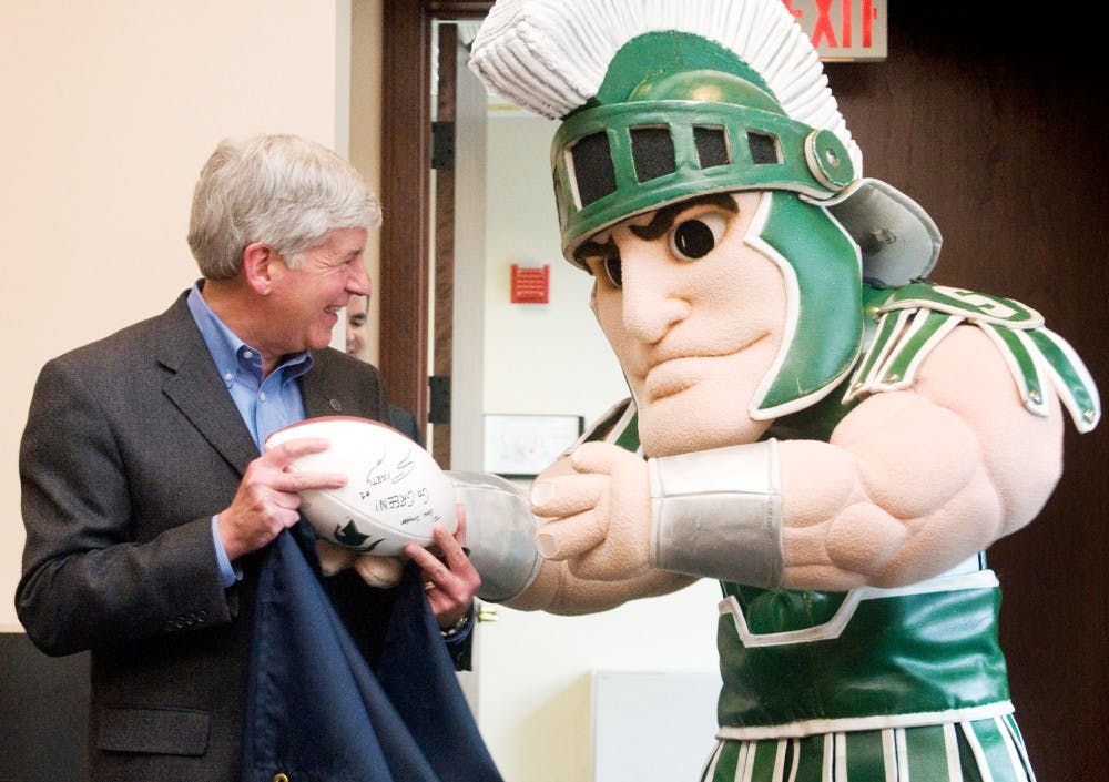 Sparty hands a football to Michigan state governor Rick Snyder Thursday at the George W. Romney Building, 111 S. Capitol Ave. in Lansing. Snyder, a University of Michigan graduate, was surprised by Sparty in anticipation of Saturday's football game. Matt Radick/The State News