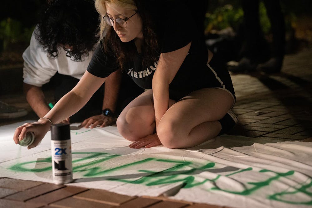 Graphic design freshman Grace Ferow sprays the word "remember" on a banner at an anniversary memorial for Michigan State Humphrey fellow and Israeli bombing victim Tariq Thabet on Oct. 30, 2024.