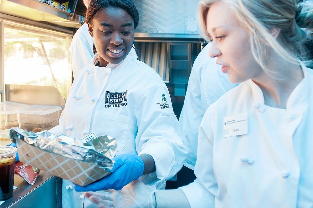 	<p>Interdisciplinary studies in social science senior Logan O&#8217;Neil, right, hands political science senior Shalah Keith a cheeseburger May 24, 2013, inside the Eat at State ON-<span class="caps">THE</span>-GO food truck outside of the Auditorium. The Smoked Cheddar Cheeseburger won an award from the National Association of College and University Food Services. Julia Nagy/The State News</p>