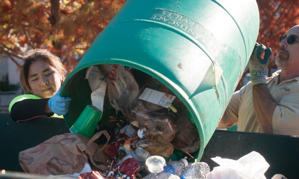 <p>From left to right, landscape gardener Sarah Greene and gardening group leader Brian Butcher throw away trash from tailgates during cleanup on Oct. 25, 2015 on the north side of campus. </p>