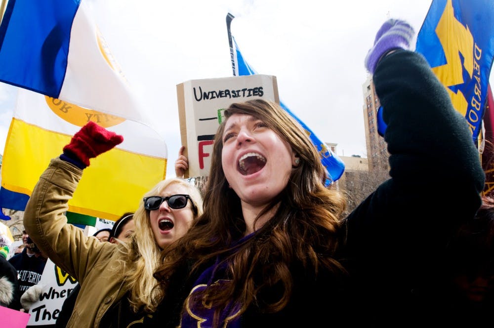 University of Michigan Dearborn students Callie Wyatt, left, and Teodora Jiga protest budget cuts Thursday afternoon in front of the State Capitol Building. Students from universities all over Michigan came together to protest governor Rick Synder's proposed budget cuts for higher education. Matt Hallowell/The State News