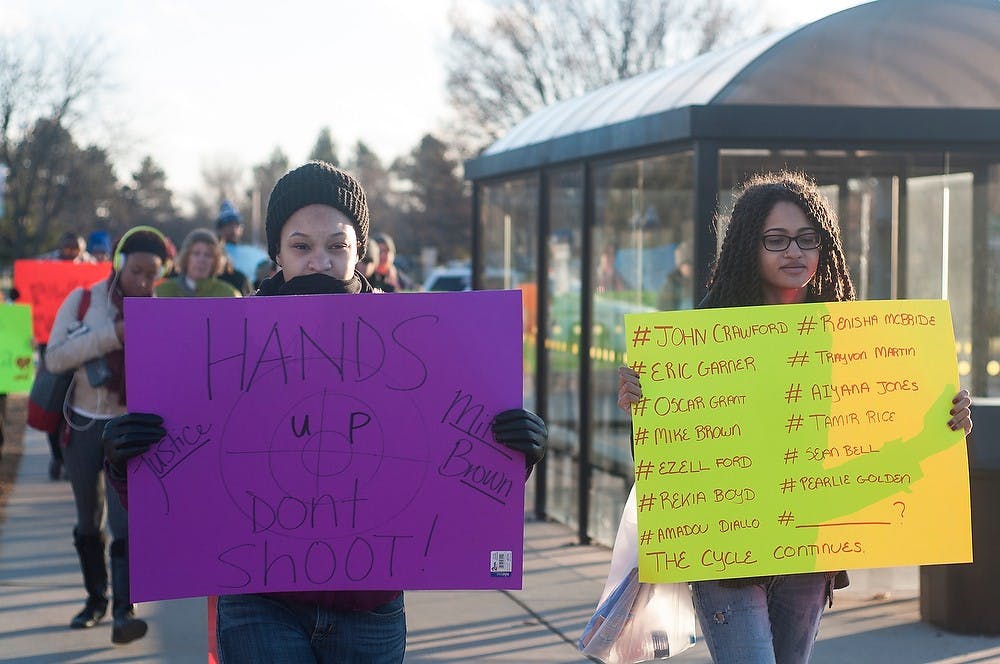 <p>Interdisciplinary studies junior Alexandria Vaughn, left, and apparel and textile design sophomore Mia Elzy, right, hold signs as they protest Dec. 03, 2014, near Conrad Hall. The NAACP held a silent march from Conrad Hall to Wilson Hall in protest of Mike Brown's death and its trial. Aerika Williams/The State News </p>