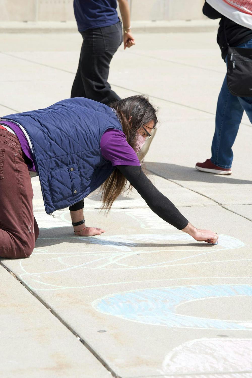A protestor writes "denounce" and "divest" on the pavement outside the MSU Breslin Center on April 26, 2024. Protestors called on MSU to divest from Israel.