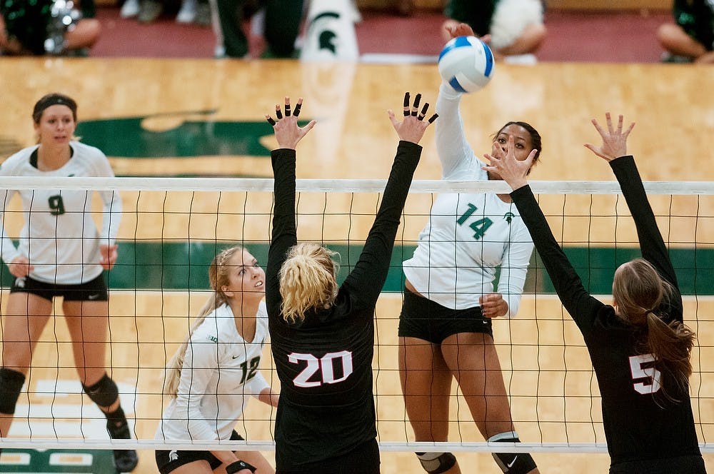 <p>Senior middle blocker/outside hitter Jazmine White spikes the ball as Nebraska middle blocker Meghan Haggerty and outside hitter Amber Rolfzen attempt to block the ball Oct. 10, 2014, at Jenison Field House. The Cornhuskers defeated the Spartans, 3-1. Aerika Williams/The State News</p>