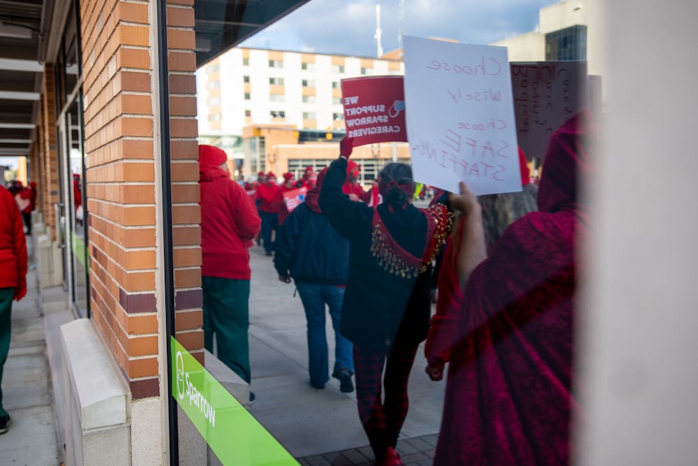 Sparrow nurses along with supporters of them picket along Michigan Avenue in Lansing on Nov. 3, 2021. Shown is a reflection off the Sparrow Urgent Care window of people at the event.  