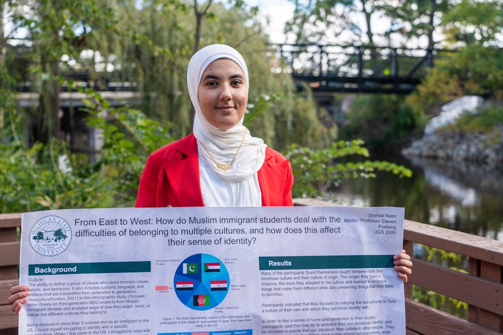 <p>Neuroscience second-year Shahad Nasir poses with a poster displaying her research next to the Red Cedar River on Tuesday, Oct. 10, 2023. Nasir's work explored how Muslim immigrant students cope with their multicultural identities.</p>