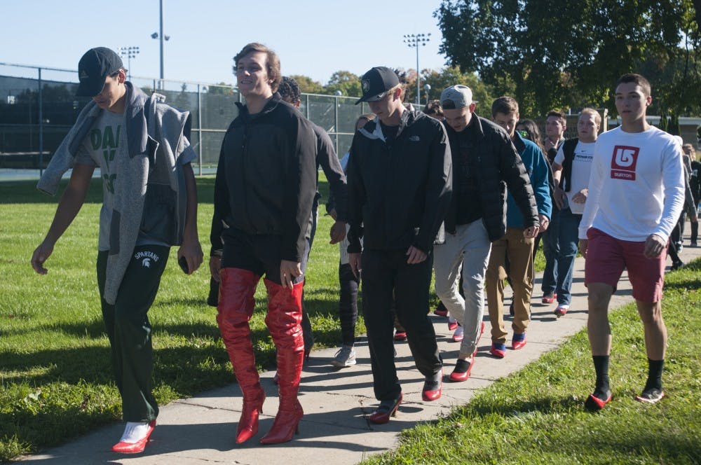 From left, Human biology freshman Joe Hannah, finance sophomore Nicholas Colucci and supply chain freshman Drew Grady walk during Alpha Chi Omega's Walk a Mile in Her Shoes event on Oct. 9, 2016 near East Lansing High School. The heels are meant to help raises= awareness about domestic violence.