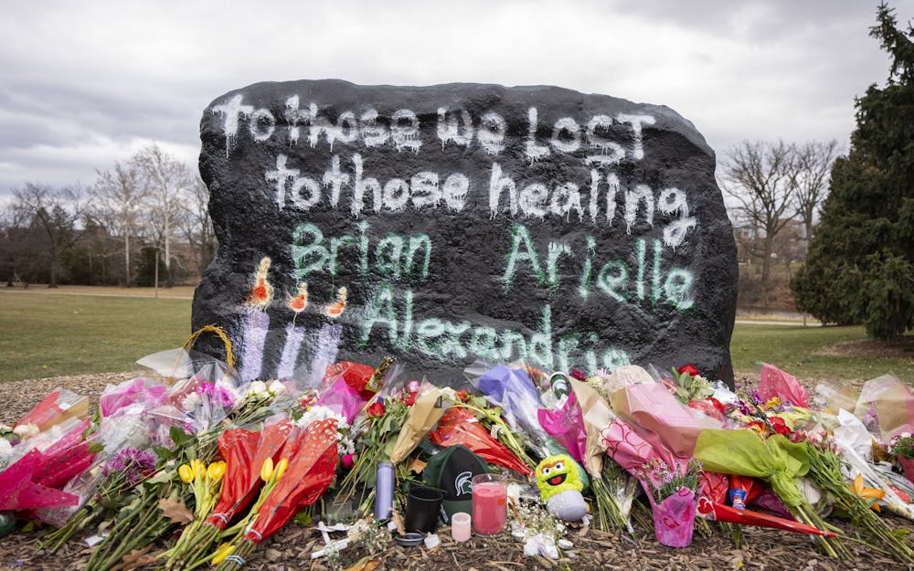 Flowers rest at the foot of the Rock on Farm Lane on Wednesday, Feb. 15, 2023 - two days after the mass shooting in Michigan State University’s north campus. Memorials have spread across campus in honor of Brian Fraser, Alexandria Verner and Arielle Anderson, the three killed on Feb. 13. 