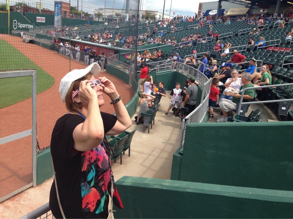 <p>&nbsp;Anne Paquet-Howard, who graduated from MSU 47 years ago, watches the eclipse as it peeks out of cloud cover at the Lansing Lugnuts game on Aug. 22, 2017.&nbsp;</p>
