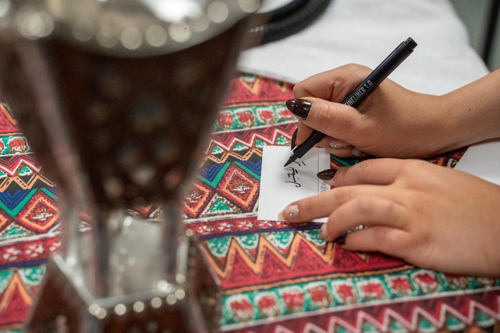 The Kuwaiti Student Organization writes a visitor’s name in Arabic at their table during the Global Festival in the International Center on Nov. 16, 2024.