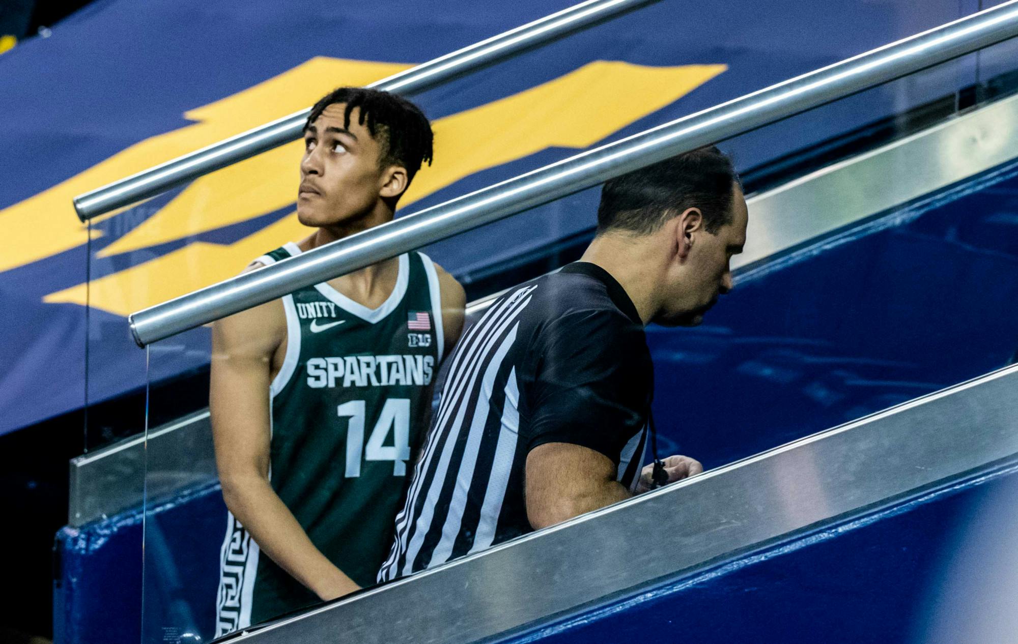 <p>Freshman guard Davis Smith (14) watches Michigan celebrate their win as he walks into the visitor locker room. The Wolverines crushed the Spartans, 69-50, at Crisler Center on Mar. 4, 2021. </p>